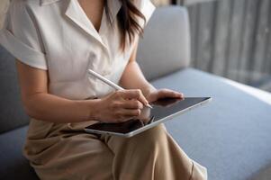 un recortado imagen de un mujer de negocios utilizando su digital tableta en un sofá en un cafetería. foto