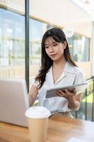 An attractive Asian businesswoman multitasks, using her digital tablet and laptop computer in office photo