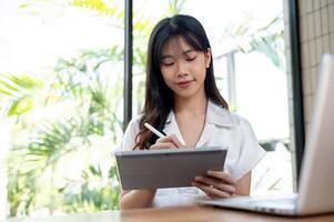 A beautiful Asian businesswoman using a stylus pen on her digital tablet, working in the office. photo