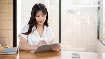 A beautiful Asian businesswoman is working on her digital tablet, writing with a stylus pen. photo