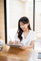 A beautiful Asian businesswoman is working on her digital tablet, writing with a stylus pen. photo