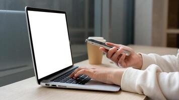 A woman working remotely at a coffee shop, working on her laptop and using her smartphone. photo