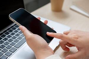 A close-up image of a woman using her smartphone at her office desk, checking messages. photo