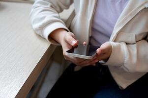 A close-up image of a woman in casual wear using her smartphone at a table indoors. photo