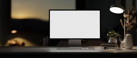 A white-screen computer mockup and a dim light from a lamp on a table in a modern dark office. photo