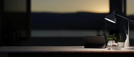 A modern dark office at night features a digital tablet and a dim light from a lamp on the table. photo