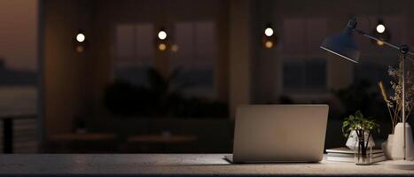 A table features a laptop computer and a dim light from a lamp in a dark coffee shop at night. photo