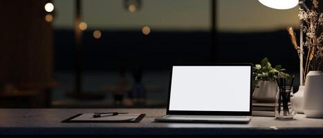 A modern dark office at night featuring a white-screen laptop computer mockup on a table. photo