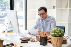 An experienced senior Asian male interior designer or architect is working at his desk in the office photo