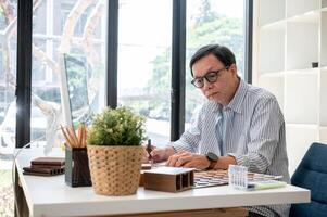 An experienced senior Asian male interior designer or architect is working at his desk in the office photo