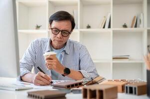 A senior male interior designer is sipping coffee while working on his project in the office. photo