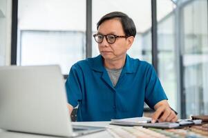 experto mayor asiático masculino interior diseñador es comprobación el edificio interior diseño en su computadora. foto