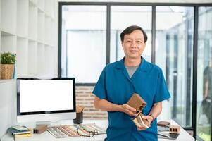 A senior Asian male interior designer with material samples in his hand is standing in his office. photo