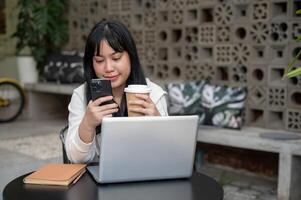 A woman is sipping coffee and watching videos on her phone while working remotely from a coffee shop photo