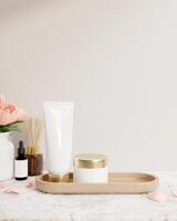 A lotion tube and a facial cream jar mockup are on a white marble tabletop against the white wall. photo