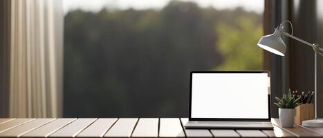 A laptop computer mockup and accessories on a wooden tabletop against the window with a nature view. photo