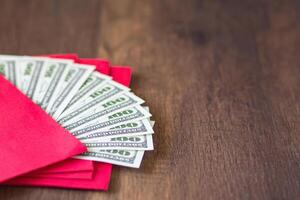 Close-up of red envelopes packet with US banknotes or Ang Pao prepare for giving to children in Chinese New Year. Wooden table background and space for text. Festival concept photo