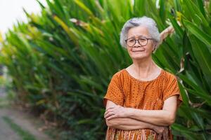 retrato de mayor mujer con corto blanco pelo en pie sonrisa y mirando a el cámara en jardín. asiático antiguo mujer sano y tener positivo pensamientos en vida hacer su contento cada día. salud concepto foto