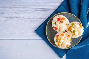 Top view of Thai steamed cupcakes topped with dry fruit on a plate on a blue cloth with a wooden background. Space for text. Khanom Pui Fai in Thai photo