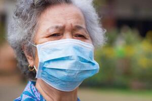 Portrait of a senior wearing a face mask and looking away while standing in a garden. Mask for protection of Covid-19, virus, coronavirus, etc. Concept of aged people and healthcare photo