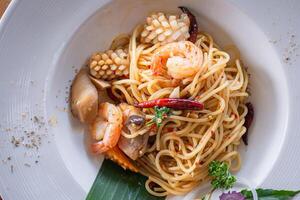 Top view of spicy stir-fried spaghetti with seafood on a white plate on the table photo