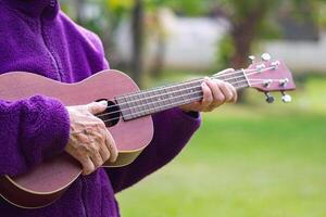 Close-up of hands senior woman holding the ukulele while standing in a garden. Space for text. Concept of aged people and relaxation photo