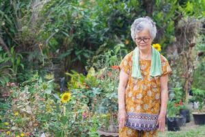 retrato de un mayor mujer ejercicios, sonriente y mirando abajo mientras en pie en un jardín. espacio para texto. concepto de Envejecido personas y cuidado de la salud foto