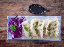 Top view of fresh Chinese dumplings or jiaozi on a plate. Chinese food with hot steams on an old wooden table photo