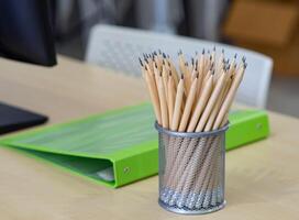 Pencils are in the mesh box, green document file placed on the desk in the workplace photo