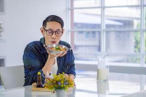 Young man wearing glasses sitting looking at the fried egg served on a pan with colorful toppings served on the pan egg. photo