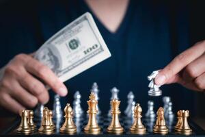 Front view of a chess game with blur background. Close-up of young man hand holding dollar currency playing chess. Business game competitive strategy. Concept of strategy for business photo