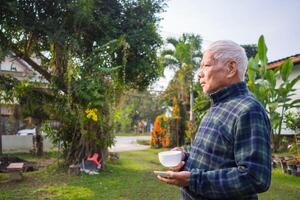 Portrait of an elderly Asian man holding a coffee cup while standing in a garden. Space for text. Concept of aged people and healthcare photo