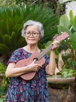 retrato de un mayor mujer jugando ukelele mientras en pie en jardín foto