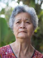 Senior woman with short gray hair face worried and looking up while standing in a garden. Space for text. Concept of aged people and healthcare photo