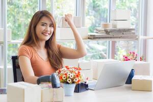 Asian businesswoman wearing casual cloth looking at the laptop and smile while sitting on a chair in the office. Space for text. Concept business and e-commerce photo