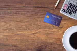 Top view of a blue credit card, pencil, calculator, a white coffee cup placed on a wooden table in the office. Space for text. Wood texture background. Business and finance concept photo