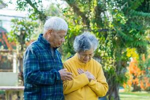 Senior woman suffering from chest pain while standing in a garden with husband. Couple senior. Concept of aged people and healthcare photo