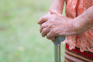 Close-up of hands senior woman holding a walking stick while standing in the garden. Space for text. Aged people and healthcare concept photo