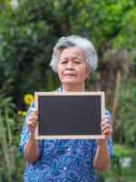 Portrait of elderly woman standing holding a blackboard and smiling in garden. Concept of old people and health care. photo