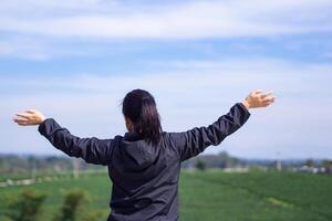 Back view of a woman hands up while standing looking at the tea plantation. Space for text. Relaxation concept photo