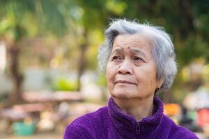 Portrait of elderly Asian woman with short gray hair and standing smiling and looking up while standing in a garden. Space for text. Concept of aged people and relaxation photo