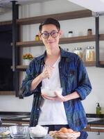 Cheerful efficient male young cook wearing casual cloth working in the kitchen. Young man worker uses whisk and bowl for making mixing ingredients in a bowl. Kitchen tools and cooking concept photo