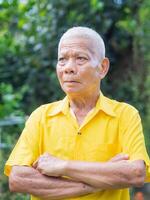 Portrait of a senior man wearing a yellow shirt, arms crossed, looking up and worried while standing in a garden. Concept of aged people and healthcare photo