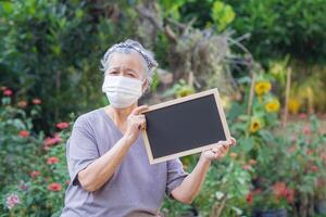 retrato de mayor mujer en pie participación un pizarra y vistiendo cara máscara para sano porque tener aire contaminación pm 2.5. máscara para proteger virus, bacterias, polen granos cuidado de la salud concepto foto