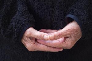 Close-up of wrinkled hands senior woman joined together for meditation. Concept of aged people and religion photo