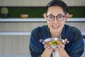 Young man wearing glasses holding a panned egg with colorful toppings served and looking at the camera. Space for text. Simple food for breakfast. Healthy foods concept photo