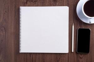 Top view of smartphone, sketchbook, pencil, and a white coffee cup on wooden table. Template for text. Wood texture background. Concept of drawing and technology photo