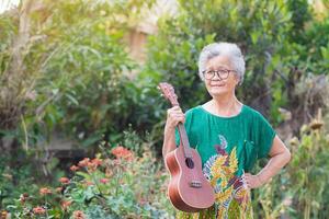 retrato de un mayor mujer participación ukelele mientras en pie en un jardín foto