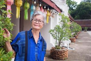 Portrait of an elderly Asian woman with short gray hair, wearing glasses, smiling, and looking at the camera while standing outdoors. Space for text. Concept of aged people and healthcare photo