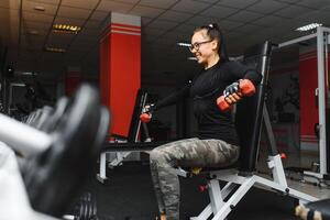 Smiling beautiful girl with heavy dumbbells in front of the mirror in a sports hall. Strong young beautiful woman is engaged in gym with dumbbells in front of a mirror photo